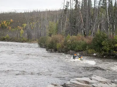 Raft paddling through a rocky rapid on a forested river