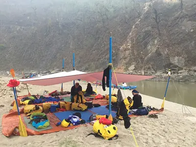 Rafters resting under a tarp shelter at a sandy riverside campsite