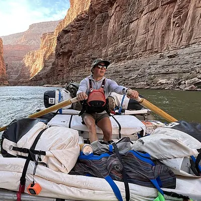 Hannah rowing a gear-filled raft between tall red canyon walls
