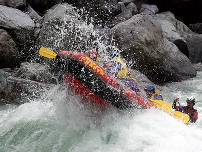 Rafters in helmets crashing through a foaming rapid between large boulders