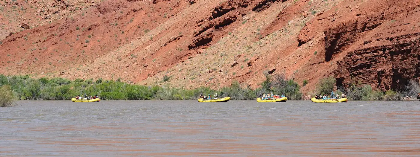 Four yellow rafts floating down a wide river beneath red canyon cliffs